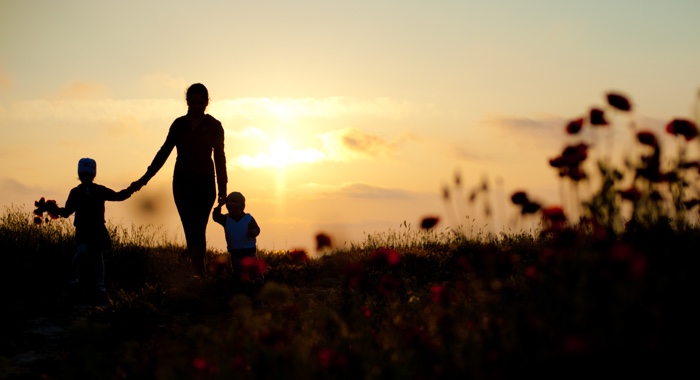 Mother holding children hands through field of flowers during sunset